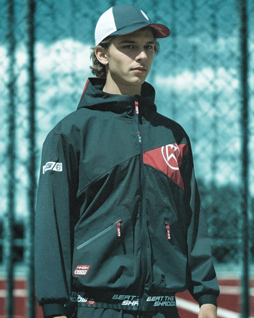 Person wearing a dark green jacket with red logo and white cap on a blurred background